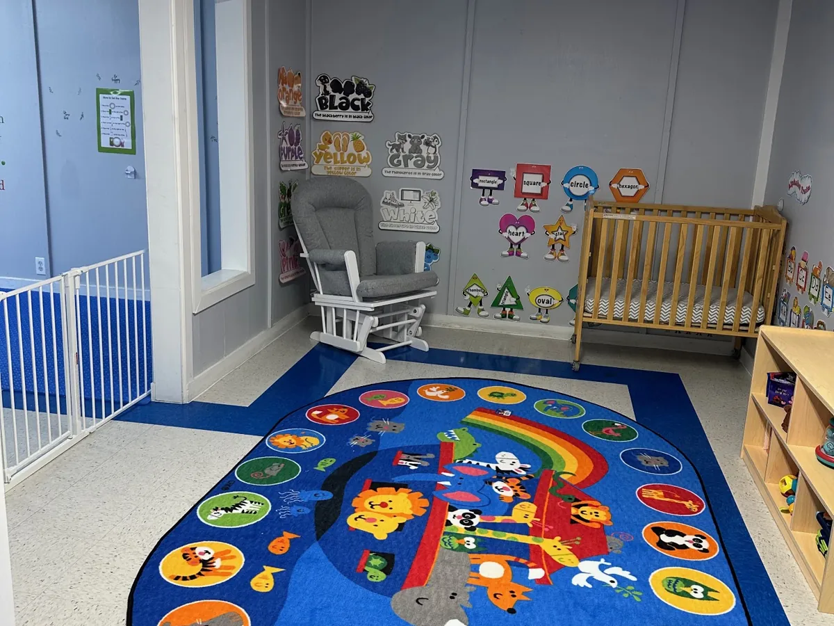 Bright classroom with a colorful alphabet rug, cribs and a rocking chair